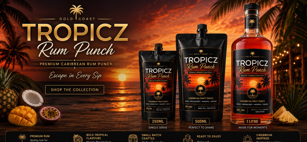Tropicz Rum Punch in three packaging sizes (250ml single serve pouch, 500ml single serve pouch, and 11L bottle) displayed against a tropical sunset beach backdrop with pineapples, mangoes, and passion fruit props.