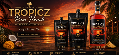 Tropicz Rum Punch in three packaging sizes (250ml single serve pouch, 500ml single serve pouch, and 11L bottle) displayed against a tropical sunset beach backdrop with pineapples, mangoes, and passion fruit props.